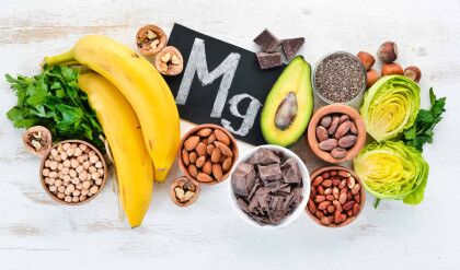 Foods containing natural magnesium. Mg: Chocolate, banana, cocoa, nuts, avocados, broccoli, almonds. Top view. On a white wooden background.