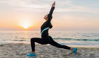 young attractive slim woman doing sport exercises on morning sunrise beach in sports wear, healthy lifestyle, listening to music on earphones, making yoga