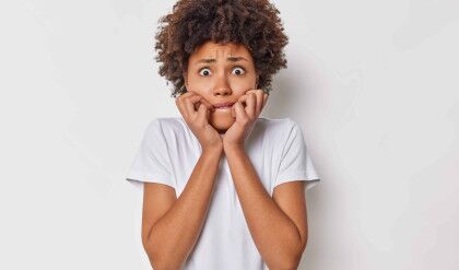 Scared nervous woman bites finger nails looks anxious at camera feels worried about something being in panic wears casual t shirt isolated over white background being afraid of terrible thing