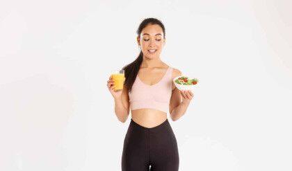 Sport, wellbeing and active lifestyle concept. Smiling healthy and slim brunette asian girl like fitness, going to gym and being on diet, holding salad with orange juice, standing white background.