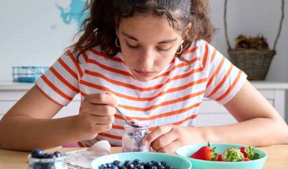 Teenage girl having a healthy breakfast with yogurt and fresh blackberries and strawberries, healthy eating concept