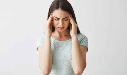 Young beautiful brunette girl frowning touching temples. Headache. Isolated on white background. Copy space.